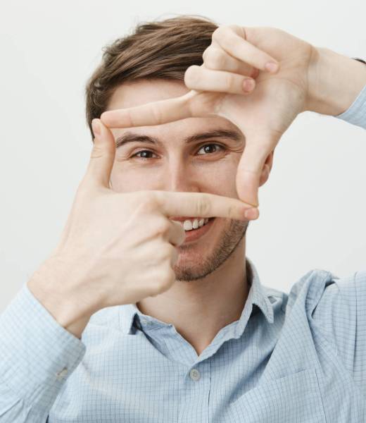 Lovely and cute boyfriend standing in feminine pose acting like girl while holding hands above chin and looking up, over gray background. Man copiying girls who sit near in cafe.